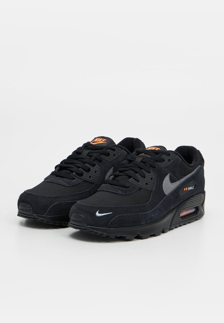 Paire de baskets Nike Air Max noires avec des accents de logo orange et un coussin d'air visible dans la semelle, sur un fond clair uni.