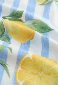 K cottontyg med ett upprepat citrondesign med gröna löv på en vit bakgrund, kompletterat av blå vertikala ränder.