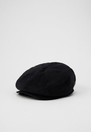 Black corduroy newsboy cap with a round, structured top, stitched detailing, and a small logo accent on the side. Flat brim design.