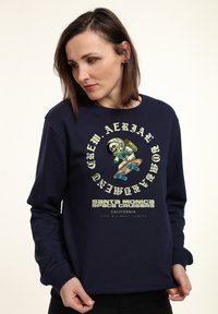 Felpa blu marina con un design grafico che presenta un teschio e un astronauta che fa skateboard, elementi testuali e polsini a costine. Materiale in cotone morbido.