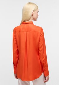 Langærmet silkjorte i klar orange; har klassisk krave, rygfold, knapmanchetter og buet nederste kant. Glat tekstur.