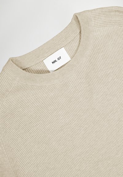 Helle beige Strickjacke mit gerippter Textur und rundem Ausschnitt. Das Etikett trägt die Aufschrift "NN. 07." Besitzt subtile Nähte entlang der Schultern.