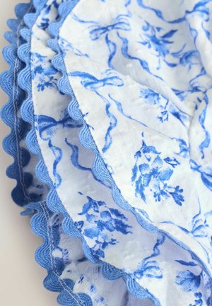 Material textil cu model floral albastru și margini ondulate, prezentând detalii intricate pe un fundal deschis. Țesătura afișată are o textură moale.