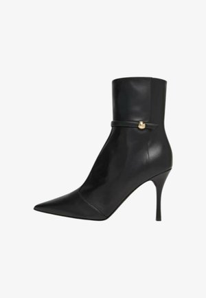 Stivaletto alla caviglia in pelle nera con punta appuntita, tacco a stiletto sottile e una cinghia stretta con dettaglio dorato intorno alla caviglia.