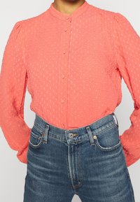 Blusa a maniche lunghe coral con motivo a pois testurizzato e bottoni rivestiti in tessuto, abbinata a jeans blue in denim a vita alta.