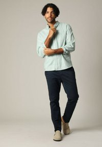 Lichtgroen overhemden met lange mouwen, marineblauwe broek en beige schoenen. Het overhemd heeft een borstzak en een relaxte pasvorm.
