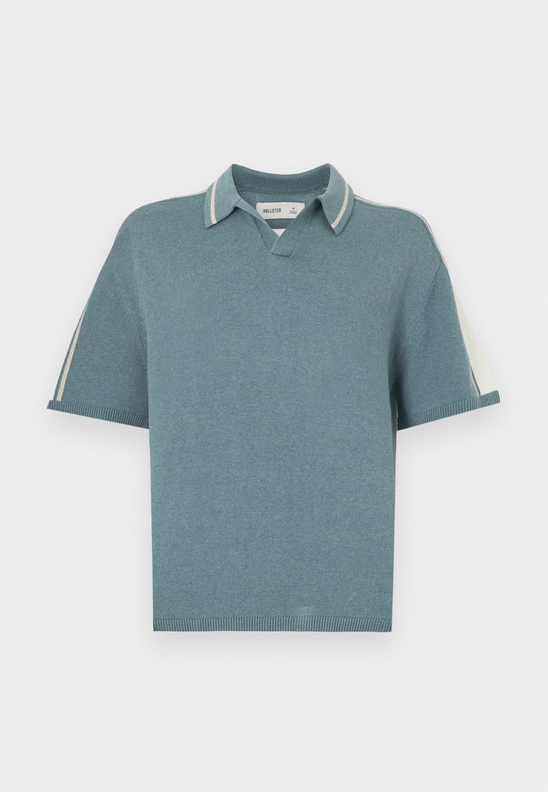 Top en maille style polo en vert d'eau doux, avec un col en V, des manches courtes et des accents de col rayés contrastants. Texture lisse sur l'ensemble.