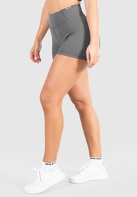 Grijze high-waisted sportshorts gemaakt van rekbaar materiaal, met een gladde textuur en minimalistisch ontwerp. Draagt witte sneakers.