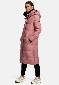 Palton lung roz, căptușit, cu glugă căptușită cu blană, având un sistem de închidere cu fermoar, buzunare laterale și o croială lejeră. Purtați peste pantaloni negri și adidași.