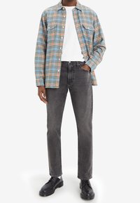 Camisa de cuadros en azul, naranja y blanco; camiseta blanca debajo. Jeans grises y zapatos negros de cordones. Corte relajado con detalle de botones.