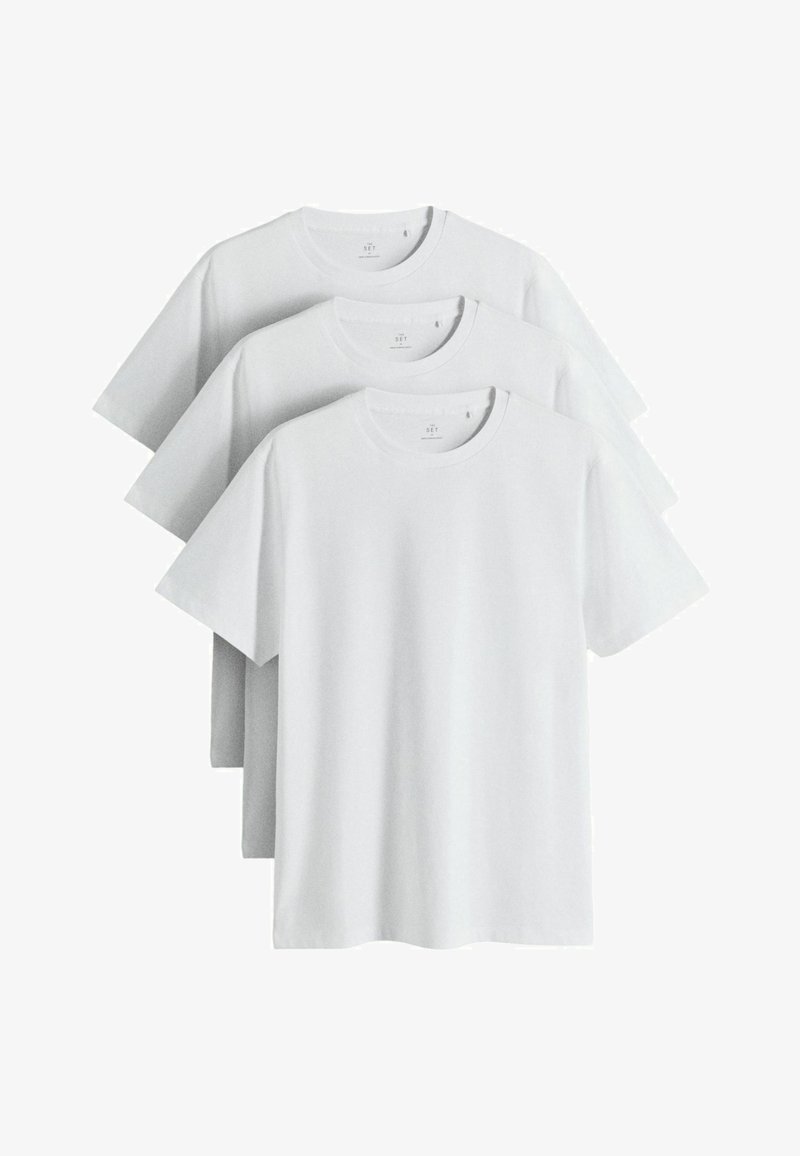 Trois t-shirts blancs unis à manches courtes et col rond empilés et présentés sur un fond blanc.