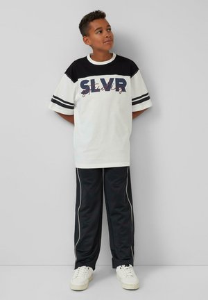 Witte en zwarte T-shirt met korte mouwen met gestreepte accenten en een "SLVR" grafiek; gecombineerd met zwarte broek met witte piping en witte sneakers.