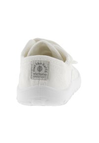 Sneaker bianca in tela con superiore in tessuto texturizzato, colletto imbottito e suola in gomma. Presenta un'etichetta con logo sul retro per identificazione.