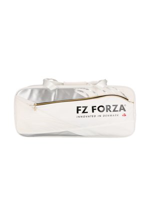 Kvinde i blåt sportstøj står med en stor hvid FZ Forza sportstaske over skulderen og kigger til siden mod en ensfarvet baggrund.
