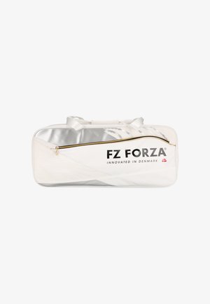Kvinde i blåt sportstøj står med en stor hvid FZ Forza sportstaske over skulderen og kigger til siden mod en ensfarvet baggrund.