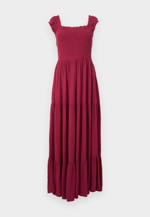 Ujjatlan bordó maxiruha fodros vállrésszel, ráncolt felsőrésszel és réteges, lebegő szoknyával, fehér háttér előtt.