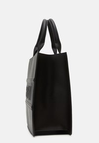 Sort tote bag med en struktureret form, glat tekstur og korte, runde håndtag. Har et subtilt logo på frontpanelet.