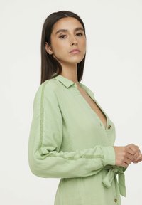 Robe vert clair en tissu texturé, dotée d'un col, de longues manches avec un bord en dentelle, de détails de boutons et d'une taille à nouer.