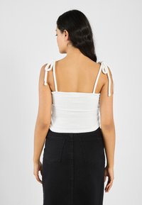Vit bomullstopp med knytband, med en figurnära design. Kombinerad med en svart denimkjol som har bakfickor och rak skärning.