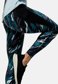 Legginsy w niebiesko-czarny abstrakcyjny wzór, z siateczkowymi panelami dla lepszej wentylacji i dopasowanym krojem. W komplecie czarne sneakersy.