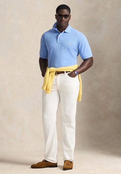 Ανοιχτό μπλε πόλο μπλουζάκι, άσπρο παντελόνι και καφέ μοκασίνια. Κίτρινο πουλόβερ δεμένο στη μέση. Γυαλιά ηλίου και ασημί ρολόι ως αξεσουάρ.