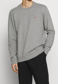 Sudadera gris de algodón, con puños y bajo acanalados, cuello redondo y un pequeño logo de bandera en el pecho.