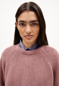Rosa gestrickter Pullover mit Rippstruktur, rundem Halsausschnitt und Raglanärmeln, über einem blauen Hemd mit Kragen und Streifen getragen.