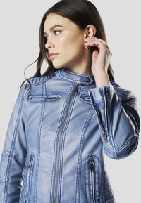 Blauwe denim motorjack met een hoge kraag, meerdere ritszakken en stikseldetails op de mouwen. Heeft een aansluitend ontwerp en een gladde textuur.