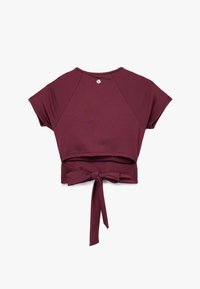Top corto burdeos con mangas cortas, con un detalle de lazo en la parte posterior y un pequeño logo cerca del escote. Hecho de tela elástica.