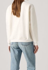 Sudadera de algodón blanca con un ajuste holgado, con puños y dobladillo acanalados, combinada con unos vaqueros desgastados de color azul claro.