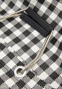 Černobílá károvaná taška vyrobená z tkaného syntetického materiálu, obsahující stříbrné kovové detaily a černé kožené akcenty na uchu.