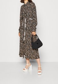 Robe noire à motifs floraux avec un col boutonné, des manches longues et un ourlet en couches, accompagnée d'un sac à main noir et de sandales à plateforme blanches.
