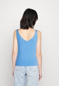 Modrý žebrovaný tílko s V-zádovým designem. Má široká ramínka a těsný střih. Nosené s světle modrými riflovými džínami s vysokým pasem.