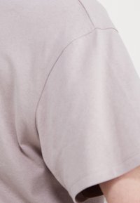 Jasnofioletowa koszula z krótkim rękawem, o miękkiej fakturze i lekko oversize'owym kroju, z widocznym szwem wzdłuż rękawa.