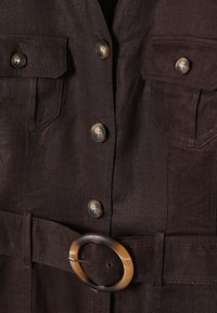 Veste en tissu marron foncé avec fermeture à boutons, poches poitrine à rabat et une ceinture assortie avec une boucle ronde en écaille de tortue.