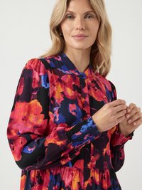 Kolorowa sukienka w kwiaty w odcieniach czerwieni, różu i niebieskiego na czarnym tle. Fafrowane rękawy z gumkami na mankietach i kołnierz zapinany na guziki.