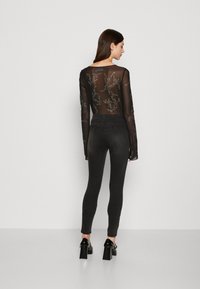 Haut transparent noir avec de longues manches brodées, associé à un legging noir taille haute et des chaussures à talons carrés. Texture lisse et design ajusté.