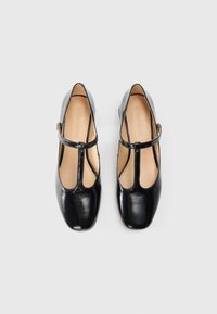 Black leather Mary Jane shoes with a sleek, square toe, T-strap design, and a low heel. Interior is light beige with embossed branding.