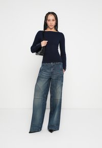 Námornícky modrý rebrovaný pletený sveter so širokým výstrihom a dlhými rukávmi, skombinovaný s nadrozmernými svetlomodrými rifľami s výrazným členením.