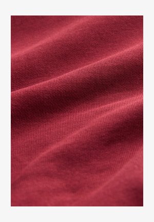 Burgundi színű anyag, sima textúrával, bordás mintával és finom fénylő felülettel, amely lágy redőkben és finom hullámzásban mutatkozik meg.
