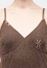 Καφέ κορυφή από διχτυωτό ύφασμα με λεπτές τιράντες, διακοσμημένη με παγιέτες σε σχέδια λουλουδιών και χάντρες στην περιοχή του στήθους.