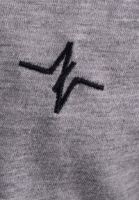 Grau Baumwollstoff mit einem schwarzen Zickzacklinien-Logo, das in der Mitte gestickt ist. Die Textur ist weich und hat ein leicht meliertes Muster.