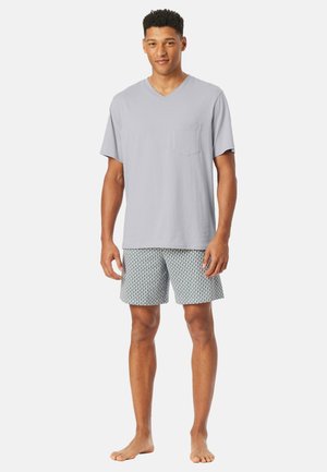 Grau v-förmiges T-Shirt mit einer Brusttasche, kombiniert mit gemusterten Shorts in Blau und Weiß. Weicher Stoff, lockere Passform und knielanger Schnitt.