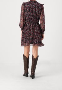 Blommig, genomskinlig, mörk klänning med långa puffärmar, rynkad midja och lagerkjol; kombinerad med höga bruna lädercowboyboots.