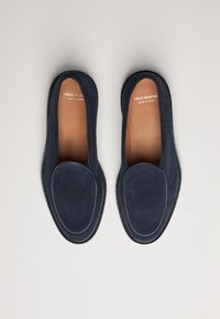 Mocasines de ante azul marino con una textura suave, punta redondeada y un ribete negro contrastante cosido. Interior etiquetado como "FRED MARTIN, HECHO EN ESPAÑA."