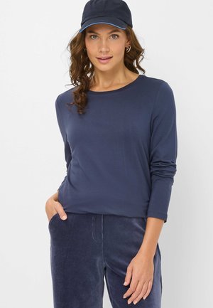 Marineblaues Langarmoberteil mit Rundhalsausschnitt, glatter Textur und lässigem Schnitt, kombiniert mit passenden Cordhosen. Mütze mit blauen Akzenten.