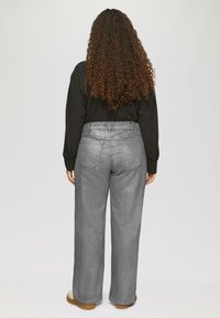 Hooggepaste, losvallende grijze jeans met een gladde textuur, vijf zakken en een klassieke knoop- en ritssluiting. Gecombineerd met een zwarte top.