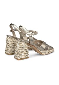 Sandali metallici oro con cinturini incrociati e tacco a blocco intrecciato beige e bianco, dotati di cinturini alla caviglia regolabili e base piatta.
