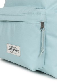 Mochila Eastpak azul claro con un diseño estructurado, textura de tela, bolsillo frontal con cremallera y un parche de logo blanco.