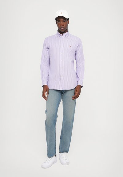 Violetinės juostelėmis dryžuota marškinėliai su sagutėmis, šviesiai mėlynos džinsinės kelnės, baltos sportbačiai ir balta kepurė. Marškinėliai turi apykaklę ir sagutes.